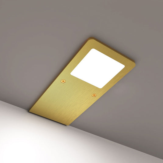 Brass cabinet light glowing natural white on a grey surface
