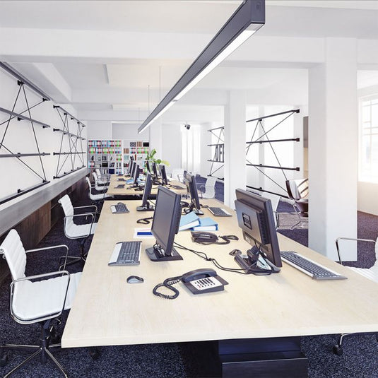 Black linear pendant lights hanging over office desks