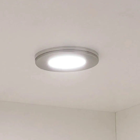 Round brushed nickel cabinet light lit under a cupboard